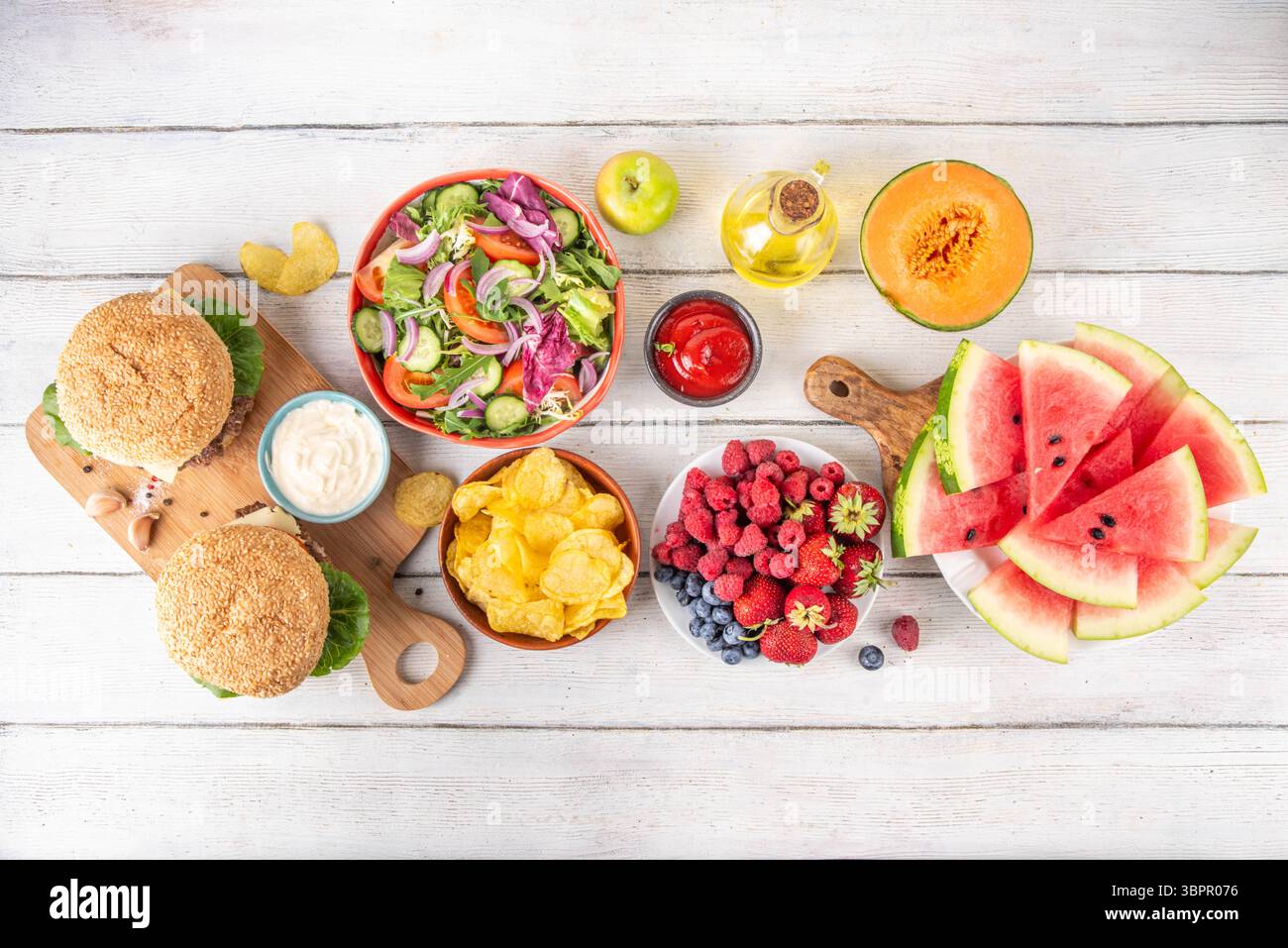 Sommer-Picknick oder BBQ-Brunch oder Mittagessen Hintergrund, leckerer Grilltisch mit Hamburger, Salaten, Obst, Wassermelone, Saucen und Snacks. Sommerfamilie und Stockfoto