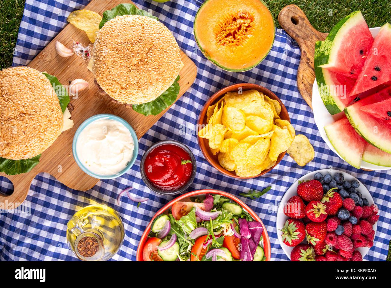 Sommer-Picknick oder BBQ-Brunch oder Mittagessen Hintergrund, leckerer Grilltisch mit Hamburger, Salaten, Obst, Wassermelone, Saucen und Snacks. Sommerfamilie und Stockfoto