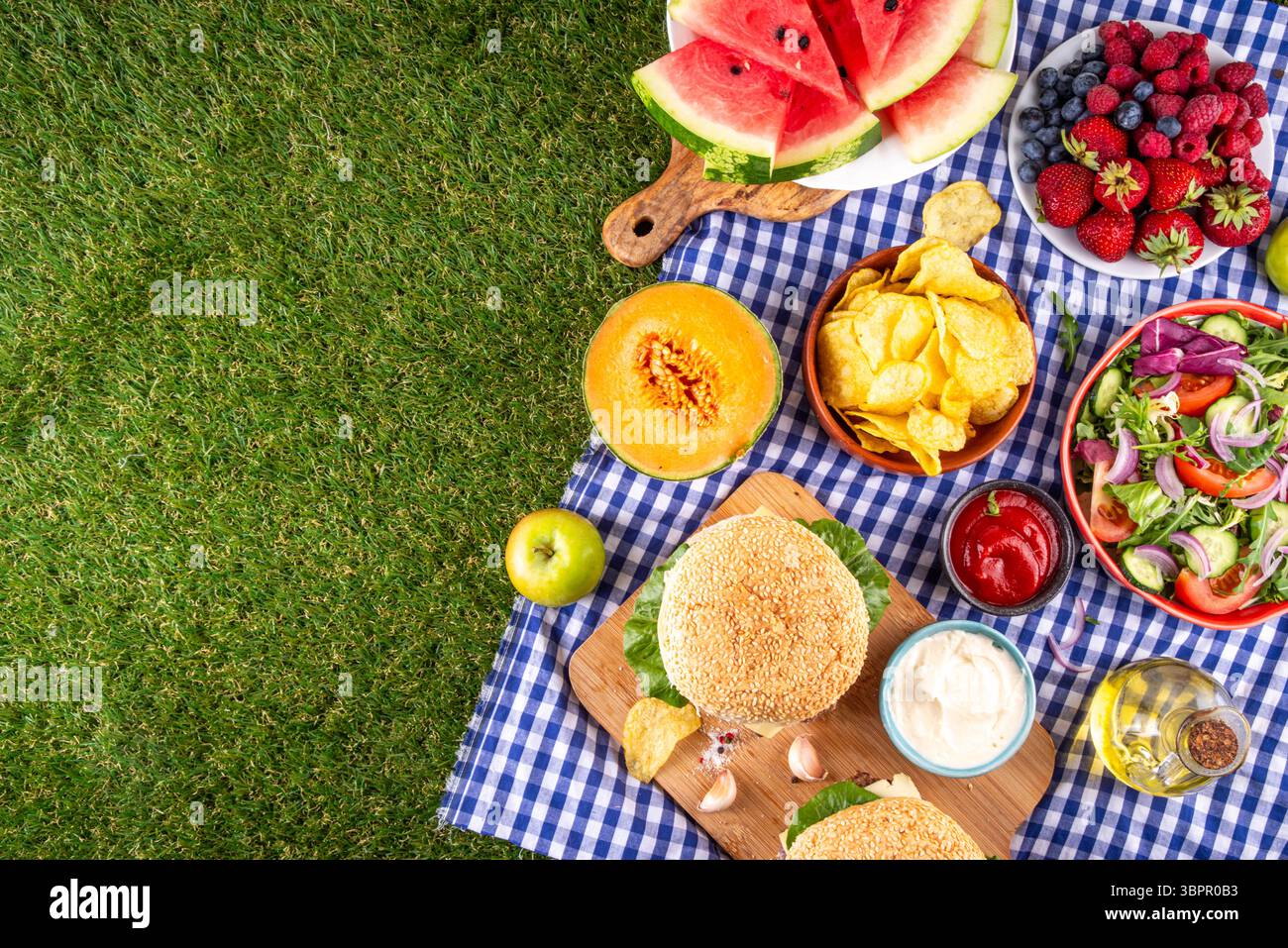 Sommer-Picknick oder BBQ-Brunch oder Mittagessen Hintergrund, leckerer Grilltisch mit Hamburger, Salaten, Obst, Wassermelone, Saucen und Snacks. Sommerfamilie und Stockfoto
