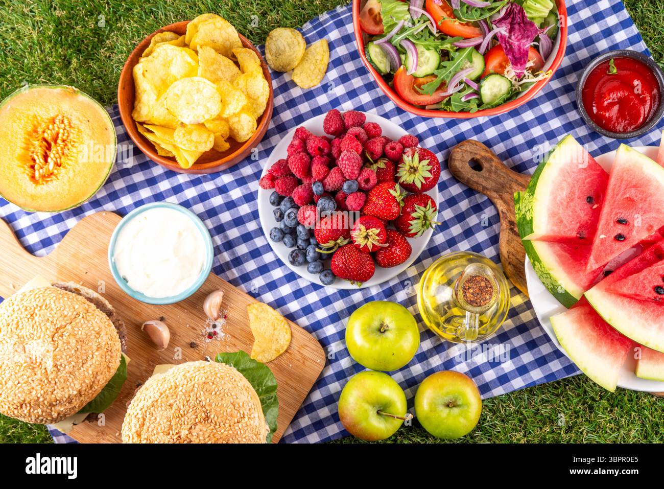 Sommer-Picknick oder BBQ-Brunch oder Mittagessen Hintergrund, leckerer Grilltisch mit Hamburger, Salaten, Obst, Wassermelone, Saucen und Snacks. Sommerfamilie und Stockfoto