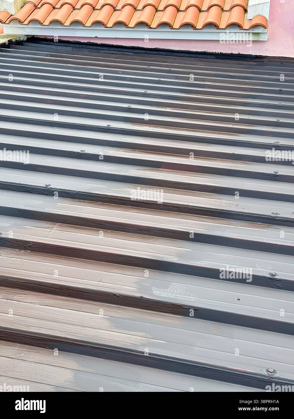 Nahaufnahme eines Wellblechdachs mit roten Keramikfliesen im Hintergrund. - Smartphone-aufgenommenes Stockfoto