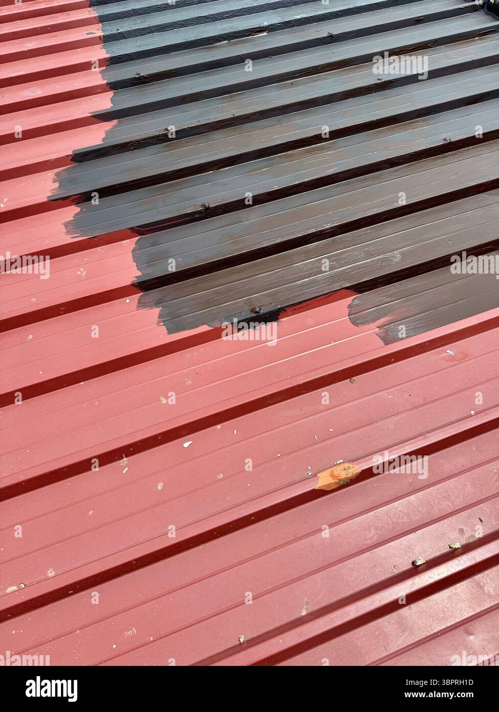 Nahaufnahme eines Wellblechdachs, das von rot nach schwarz lackiert wird, zeigt einen laufenden Übergang. - Smartphone-aufgenommenes Stockfoto