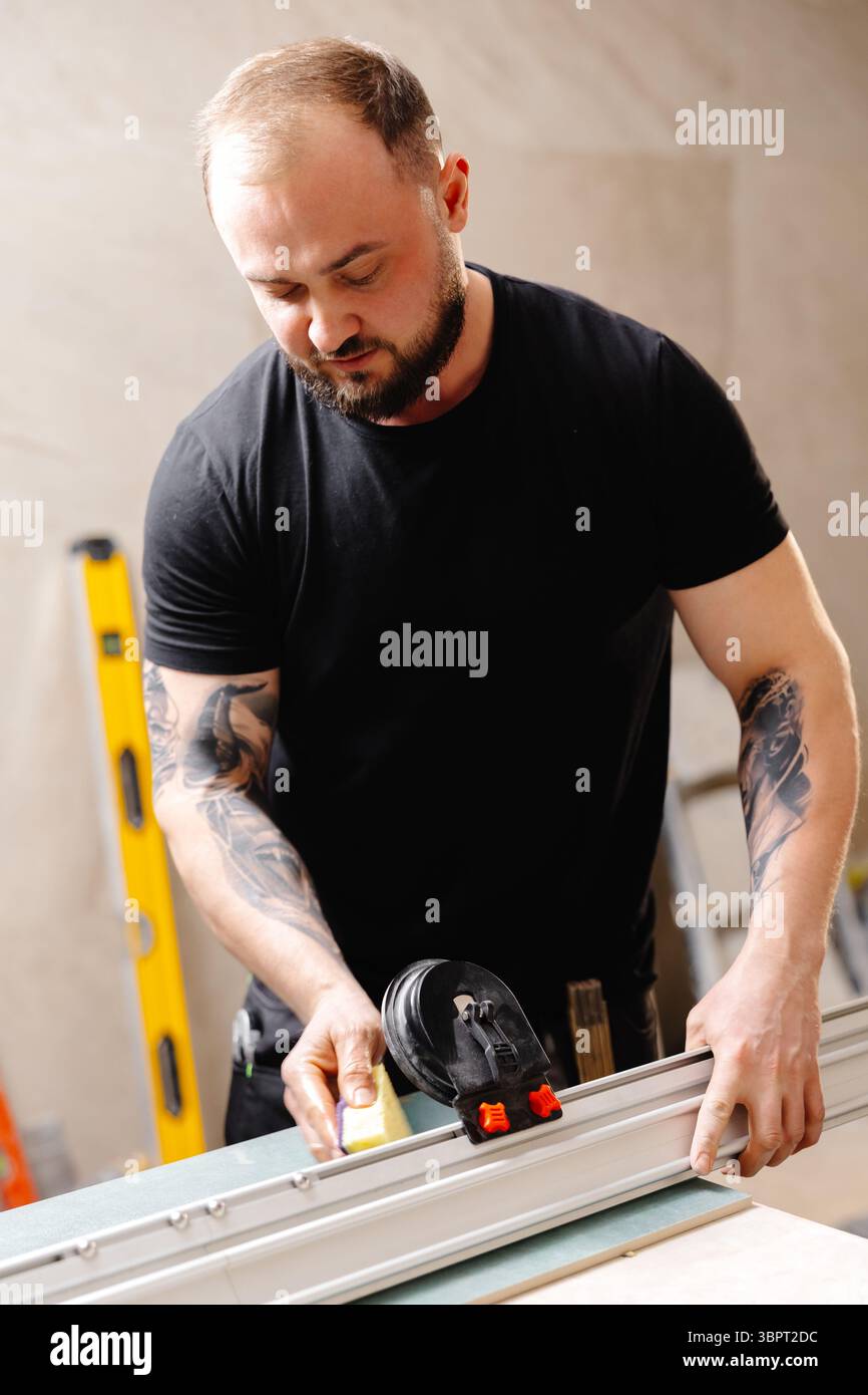 Der Baumeister bereitet Aluminiumprofile für die Dehndecke unter Verwendung spezieller Ausrüstung in der renovierten Wohnung vor Stockfoto