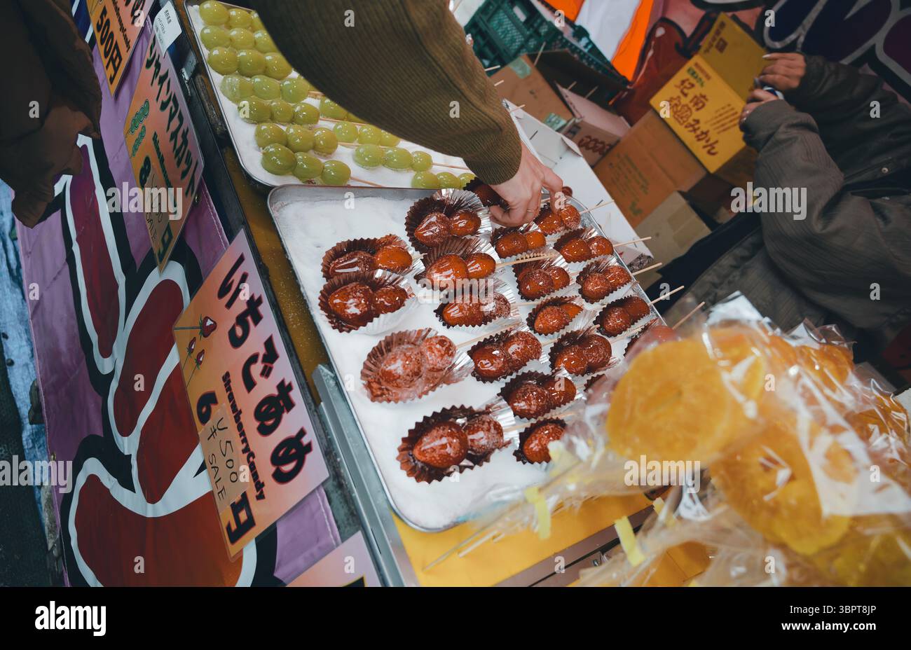 Käufer pflücken glänzende kandierte Erdbeeren und Früchte an einem Lebensmittelmarkt in Tokio Stockfoto