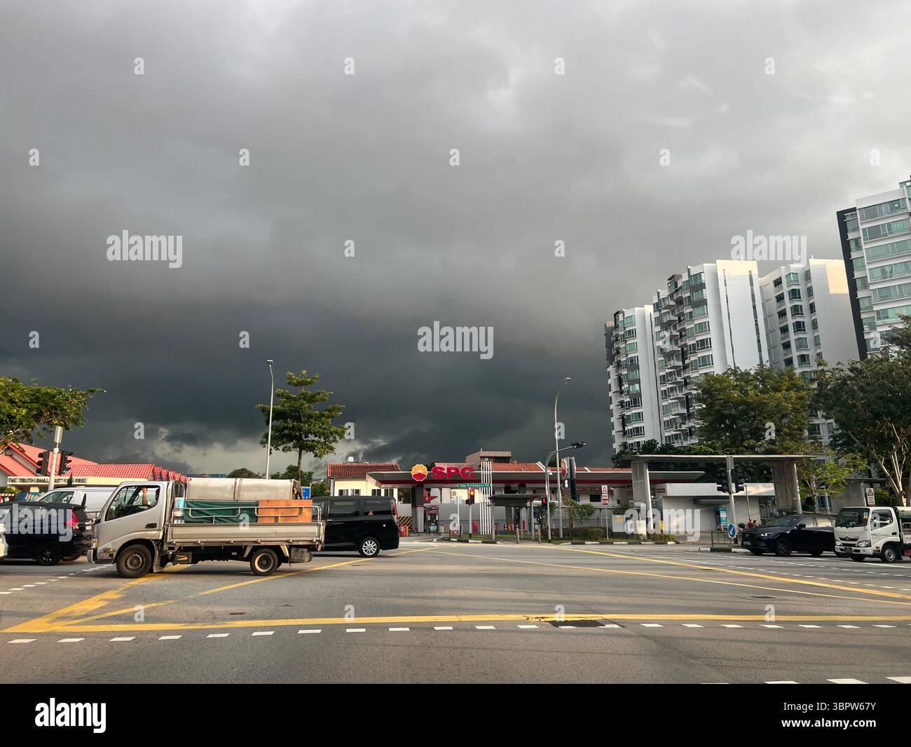 Sturmwolken sammeln sich über einer Vorstadtstraße in Singapur, mit Fahrzeugen und Wohngebäuden unter einem stimmungsvollen Himmel. - Smartphone-aufgenommenes Stockfoto
