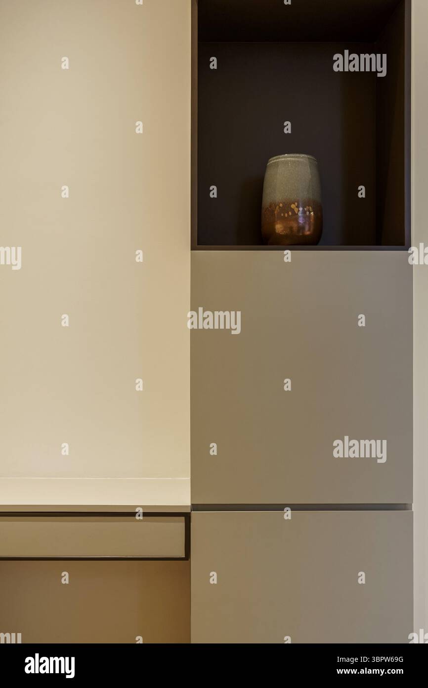 Minimalistisches Innendesign mit modernem Einbauregal und Schrank. Eine dekorative Keramikvase befindet sich in einem dunklen, vertieften Ablagefach. Leitungen und Neutralstellung reinigen Stockfoto