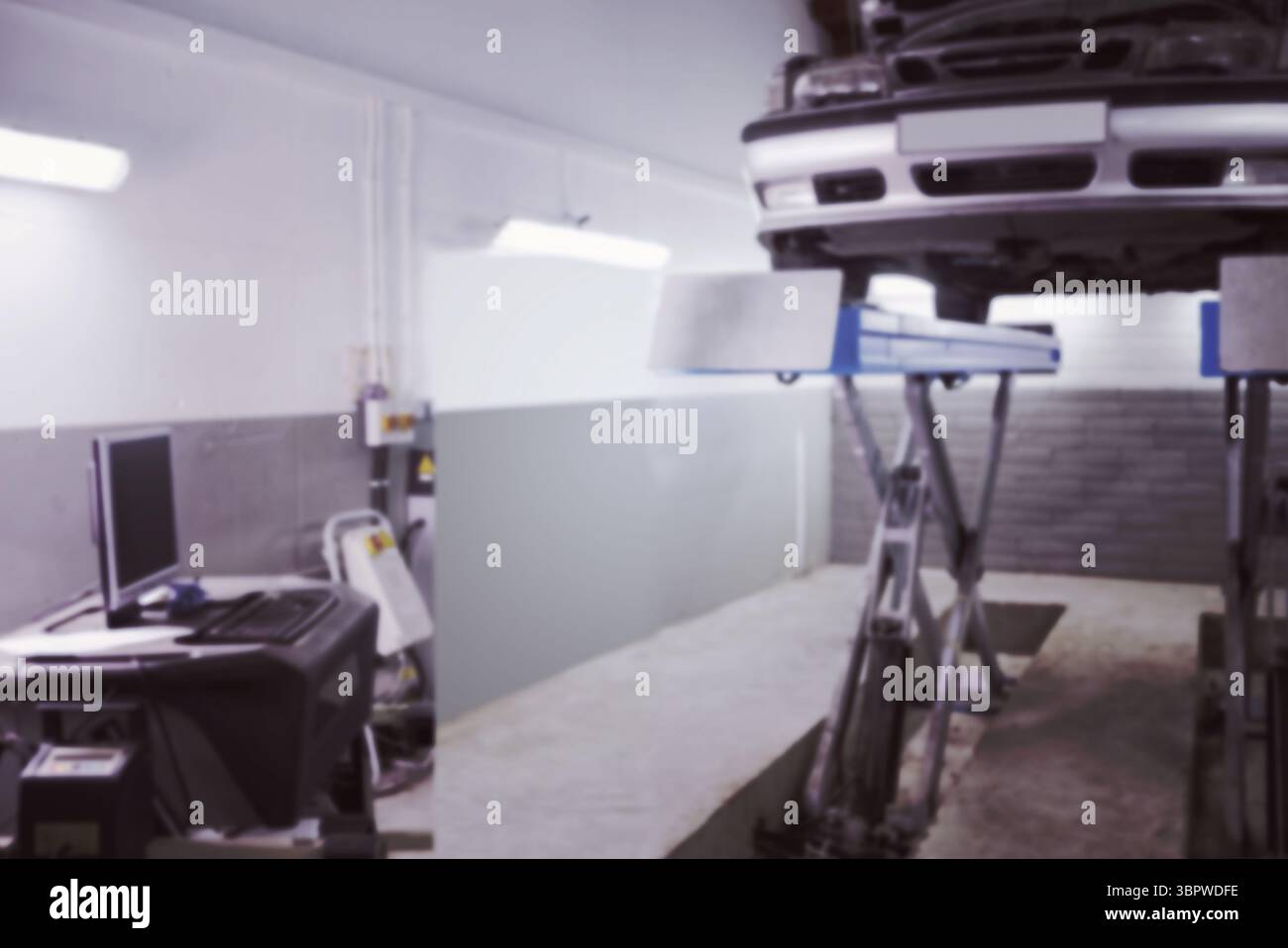 Die Vorderseite des hellen Autos wird auf einem hydraulischen Aufzug in einem flachen Shop mit Computerwagen angehoben Stockfoto