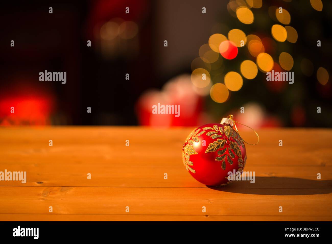 Die rote Kugel mit Blattgold liegt im 3D-Rendering auf einer hölzernen Tischplatte und leuchtet unter Bokeh Stockfoto