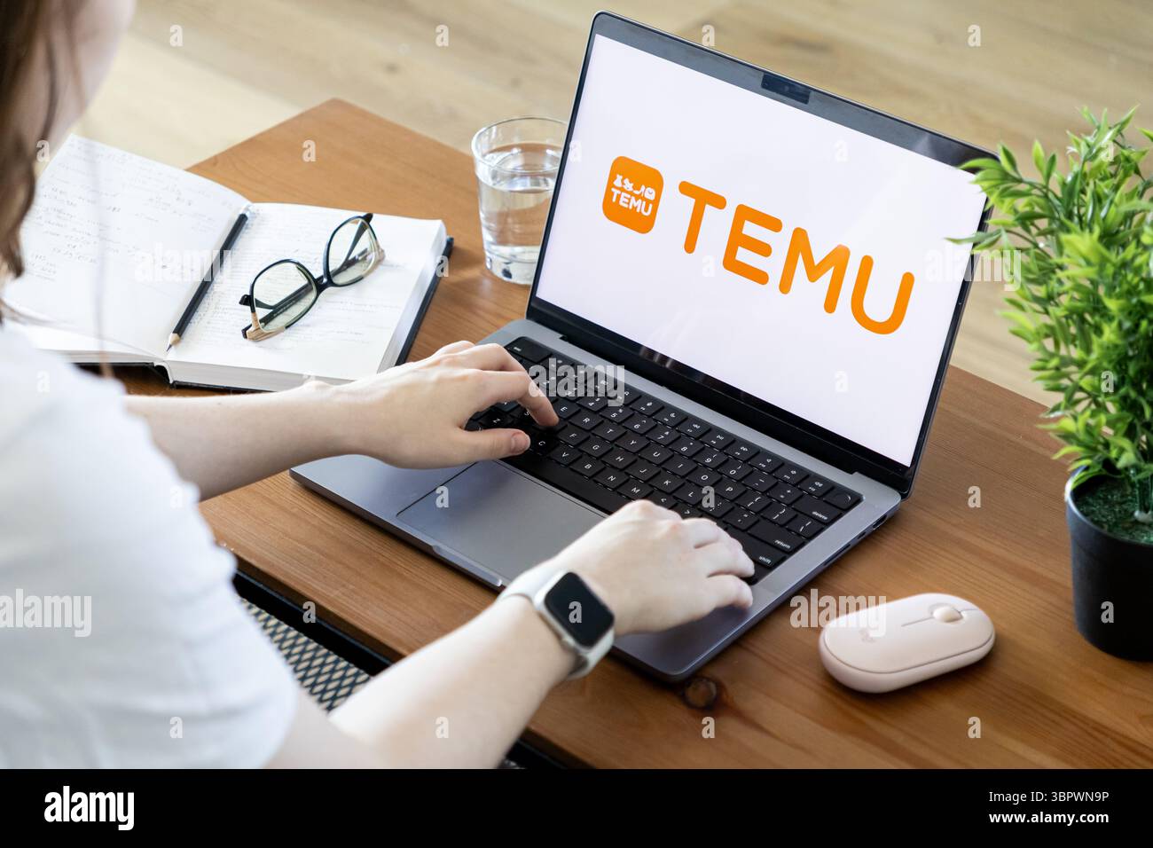 Posen, Polen – 15. Juni 2025: Die Hände einer Person tippen aktiv auf einem modernen Laptop und zeigen das Logo der Marke TEMU auf dem Bildschirm in einem Heimbüro Stockfoto