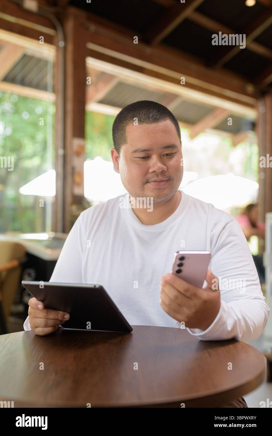 Asiatischer junger Mann in Übergröße, der im Café-Restaurant sitzt Stockfoto