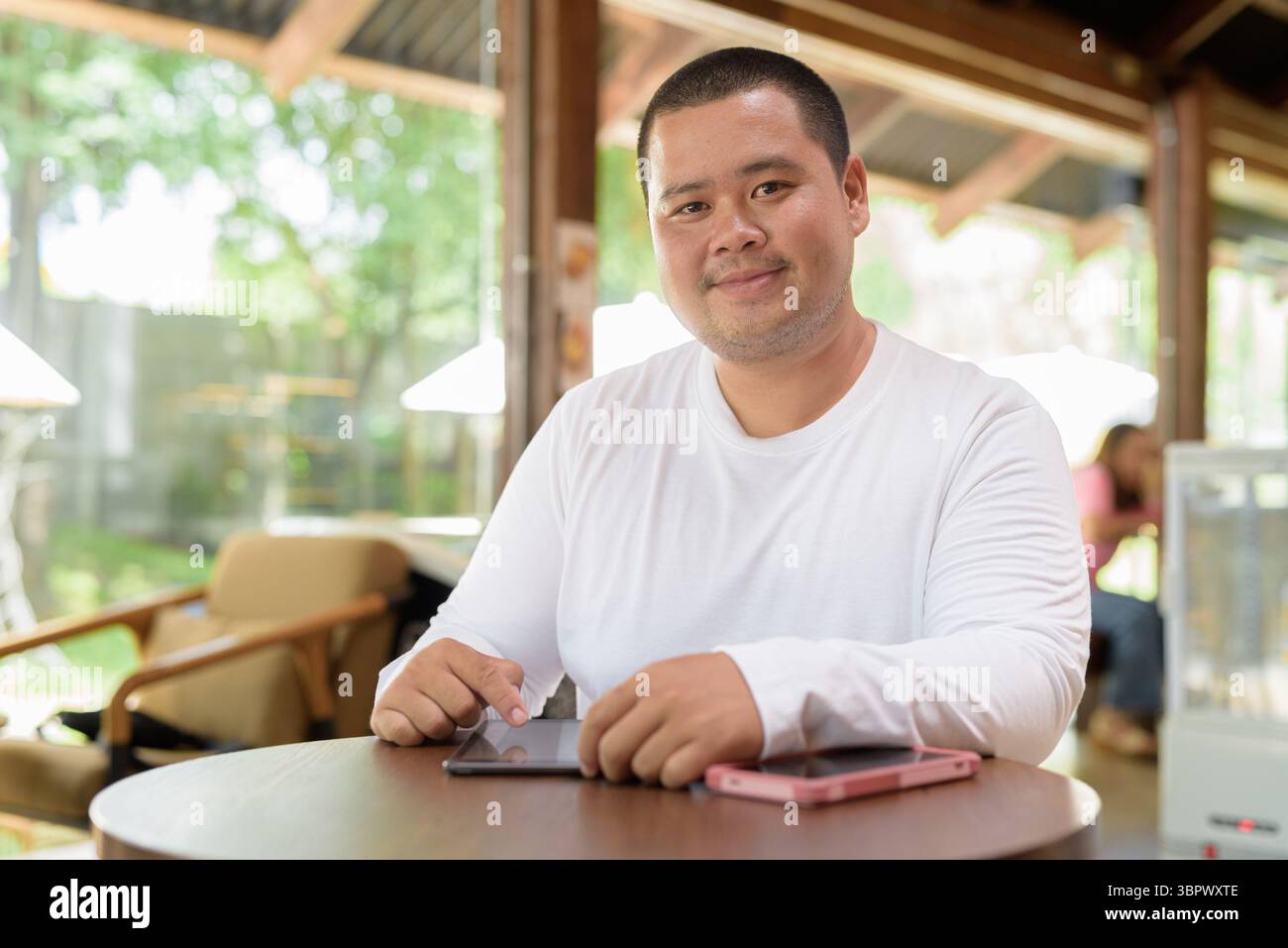 Asiatischer junger Mann in Übergröße, der im Café-Restaurant sitzt Stockfoto