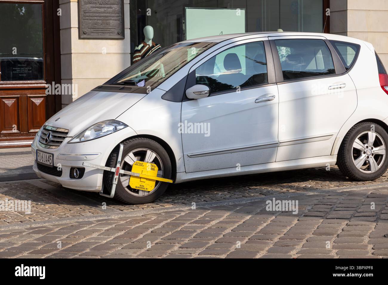 Posen, Polen - 18. Juni 2025: Weißes Auto mit einer markanten gelben Radklemme, die Folgen von Parkverstößen in der Stadt zeigt Stockfoto