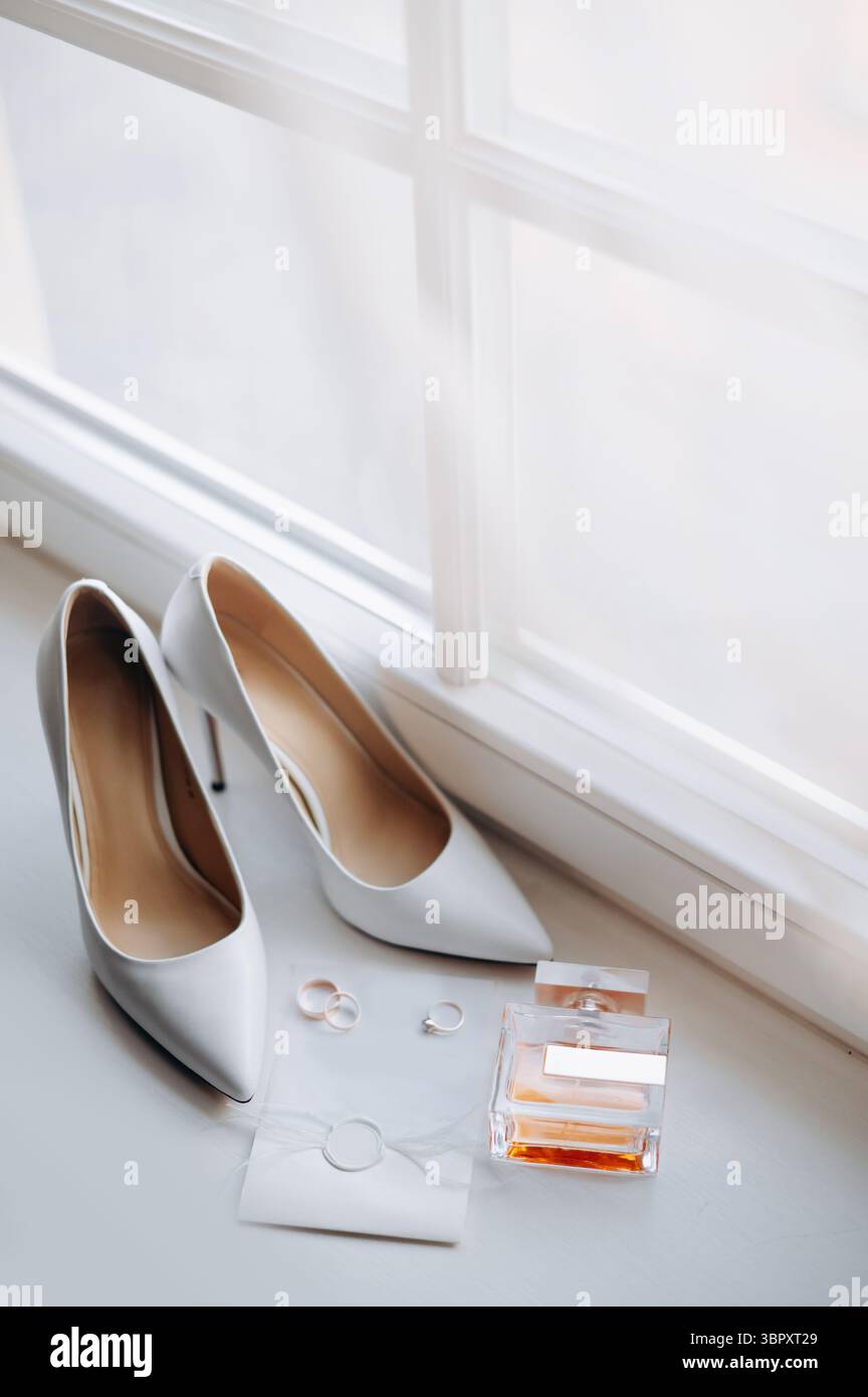 Nahaufnahme der Hochzeitsdetails. Bride Elegance Schuhe, Ringe, Parfum und Invation layflat auf weißer Fensterbank Stockfoto