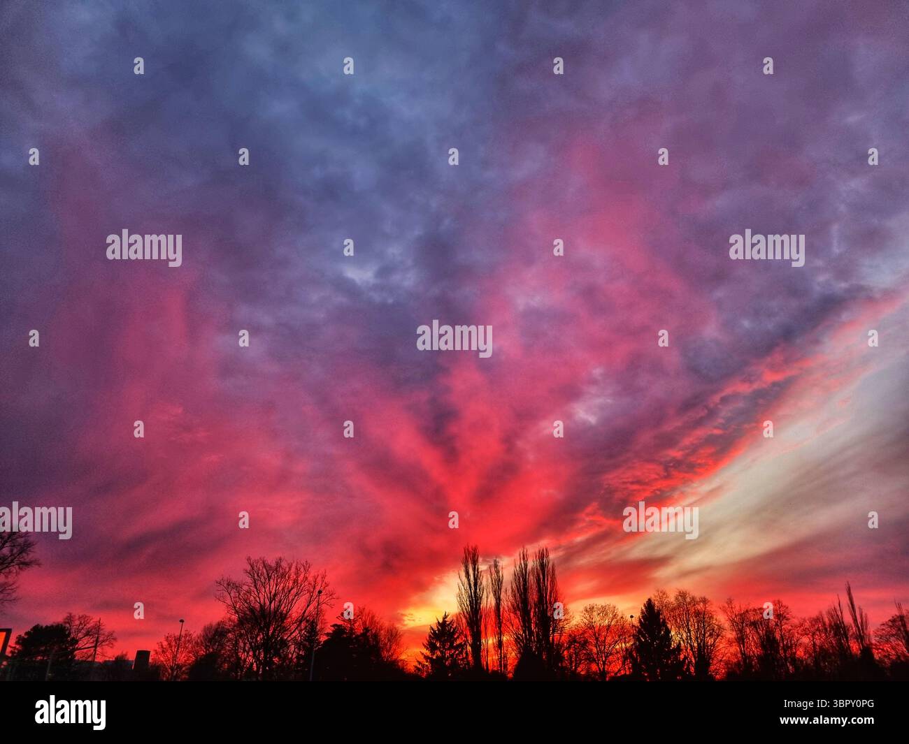 Ein unglaublich dramatischer und apokalyptischer Sonnenaufgang zeigt den Himmel in feurigen Rot- und tiefvioletten Tönen über einer dunklen Silhouette der Stadt. - Smartphone-aufgenommenes Stockfoto