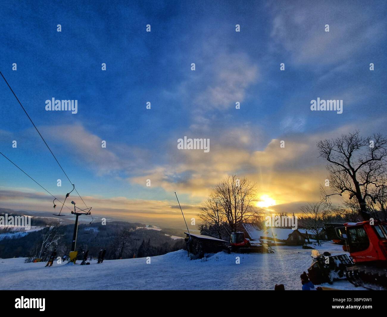 Malerische Aussicht von einer verschneiten Skipiste in den tschechischen Bergen in der Abenddämmerung, die Skilifte unter einem wunderschönen, farbenfrohen Wintersonnenuntergang mit einem Steigungshimmel zeigt. - Smartphone-aufgenommenes Stockfoto