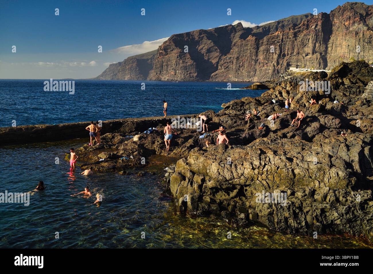 Menschen schwimmen in natürlichen Küstenbecken mit Los Gigantes Bergen und Klippen in der Ferne, Charco de Isla Cangrejo, Teneriffa, Kanarische Inseln, Spanien Stockfoto