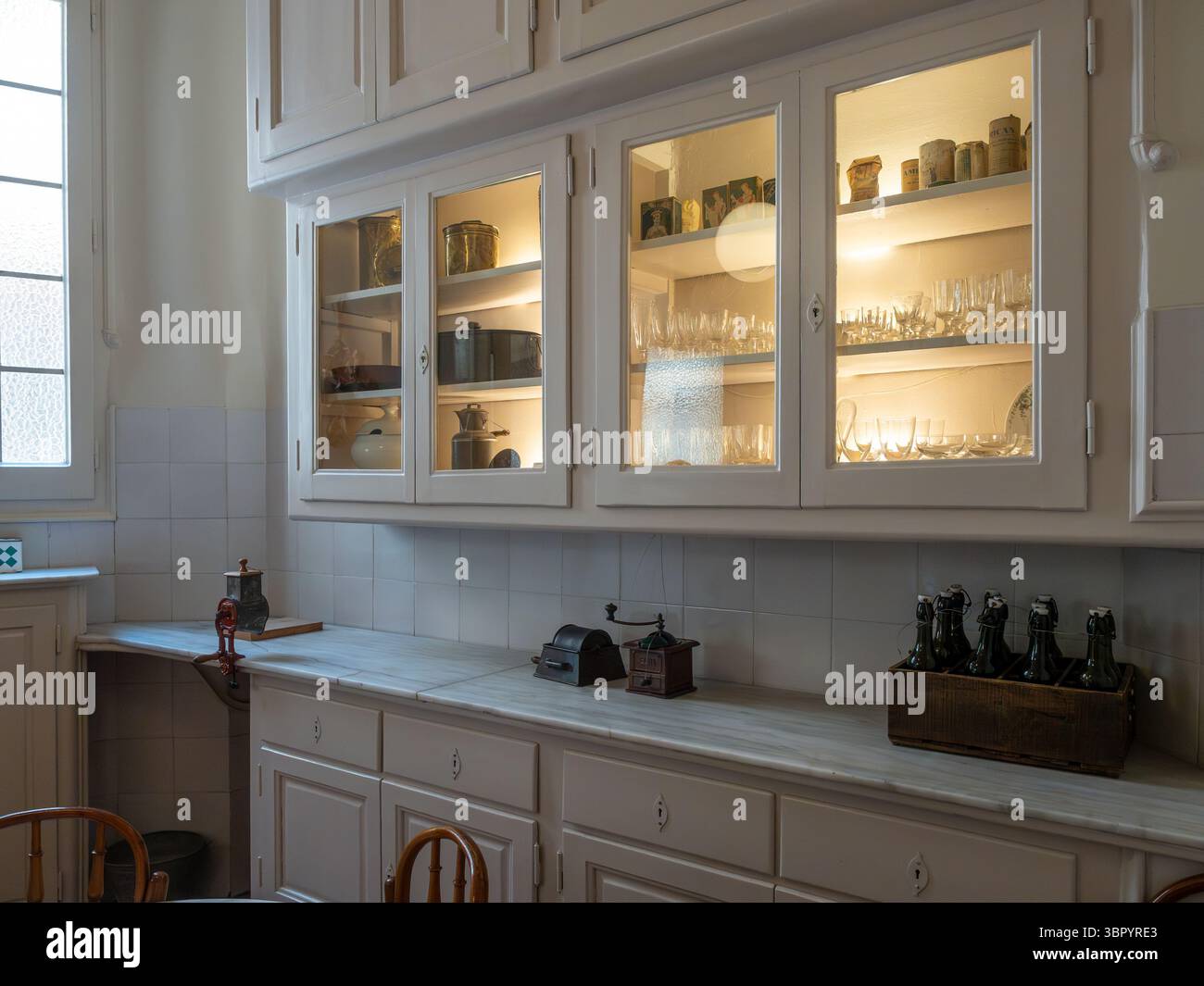Alte Glaswaren und Geschirr in einem beleuchteten Küchenschrank in der restaurierten Wohnung aus dem frühen 20. Jahrhundert in der Casa Milà, Barcelona, Spanien. Stockfoto