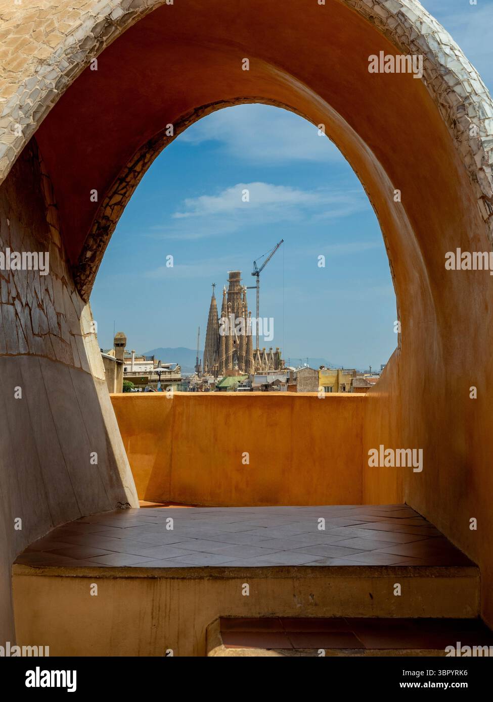 Blick auf die berühmte Basilika La Sagrada Familia, gesehen durch einen Steinbogen auf der Dachterrasse von Casa Milà (La Pedrera), Barcelona, Spanien. Stockfoto