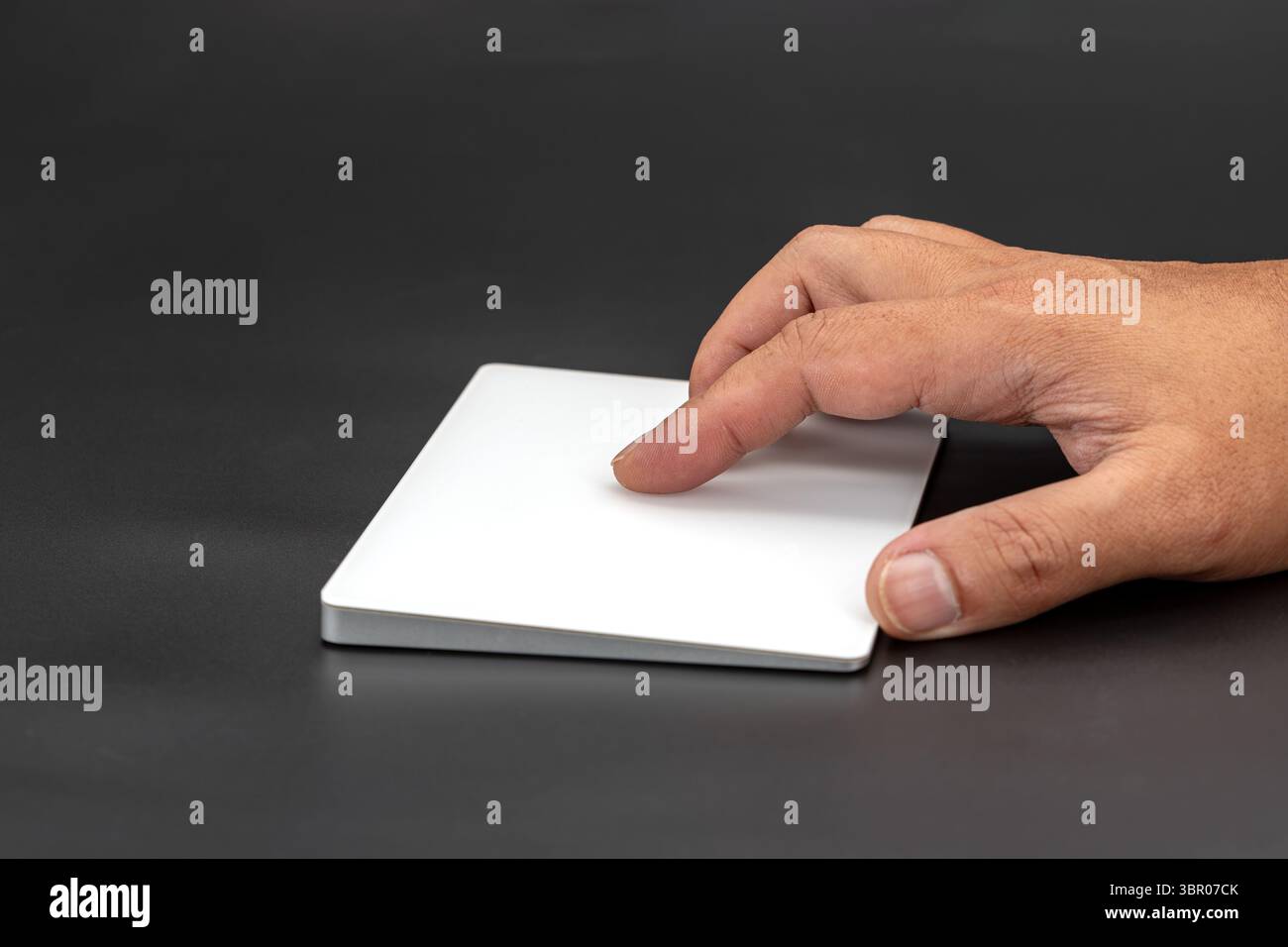 Eine Hand interagiert sanft mit dem eleganten weißen Trackpad auf dem dunklen Schreibtisch und bietet moderne Technologie und Benutzerinteraktionen. Minimalistisches Design betont Stockfoto