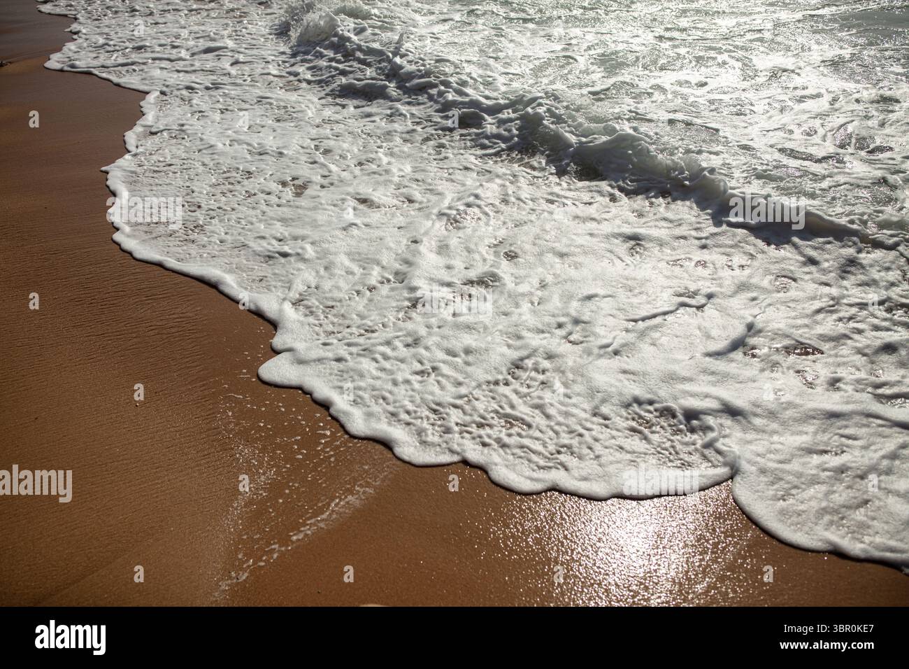 Schäumende Ocean Wave, Die Über Sandy Beach Gespült Wird Stockfoto