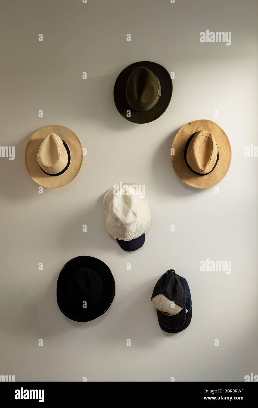 Sechs Hüte hängen in lockerer symmetrischer Anordnung an einer glatten hellen Wand im Flur. Kopfbedeckung, Mode, Accessoires, minimalistisch, Innenausstattung, dis Stockfoto