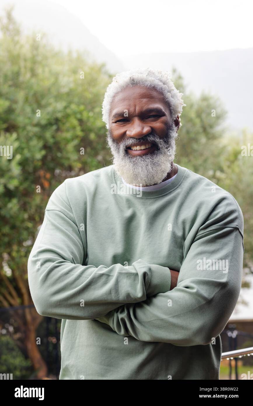 Ranghoher Afroamerikaner, der mit überkreuzten Armen steht und hellgrünes Sweatshirt im Garten trägt. Porträt, Wellness, Natur, lässig, Ruhe, li Stockfoto