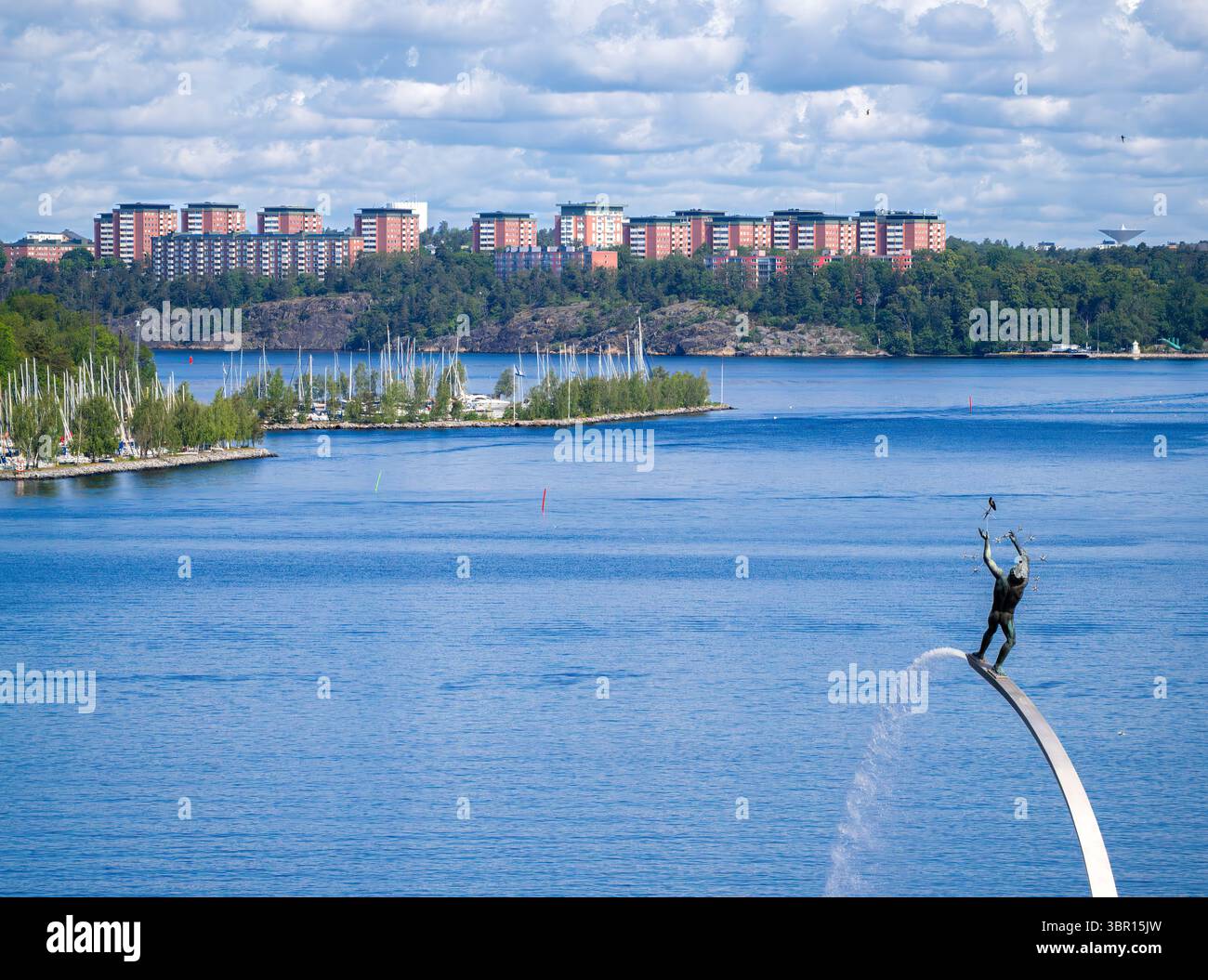 Stockholm, Schweden - 10. Juni 2025: Eine malerische Aussicht mit einer Nacka Strand Skulptur Gottes, die in einem Regenbogen steht, und einer Stadtlandschaft mit Wohnraum Stockfoto