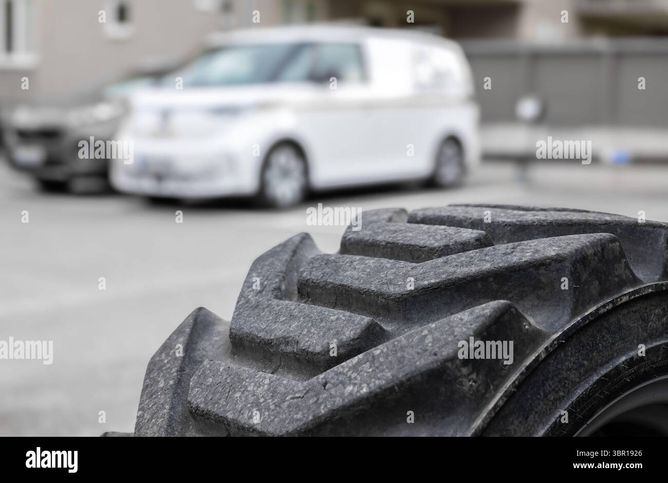 Nahaufnahme eines robusten Reifenprofils mit einem verschwommenen weißen Lieferwagen im Hintergrund, der den städtischen Nahverkehr zeigt. Stockfoto