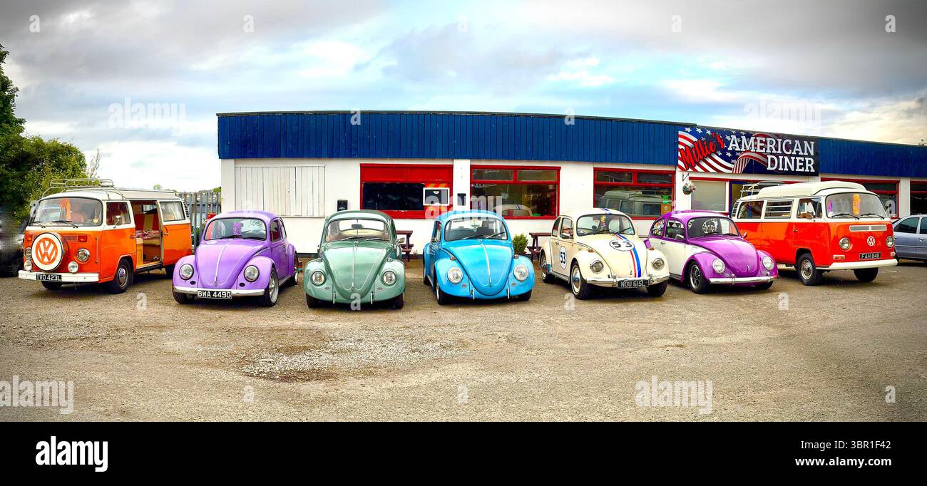 Weitwinkelpanorama einer Reihe von Vintage Volkswagen-Käfern und orangen vw-Transporter T3-Wohnwagen, die vor dem bewölkten Himmel des amerikanischen Diner geparkt sind - Smartphone-aufgenommenes Stockfoto