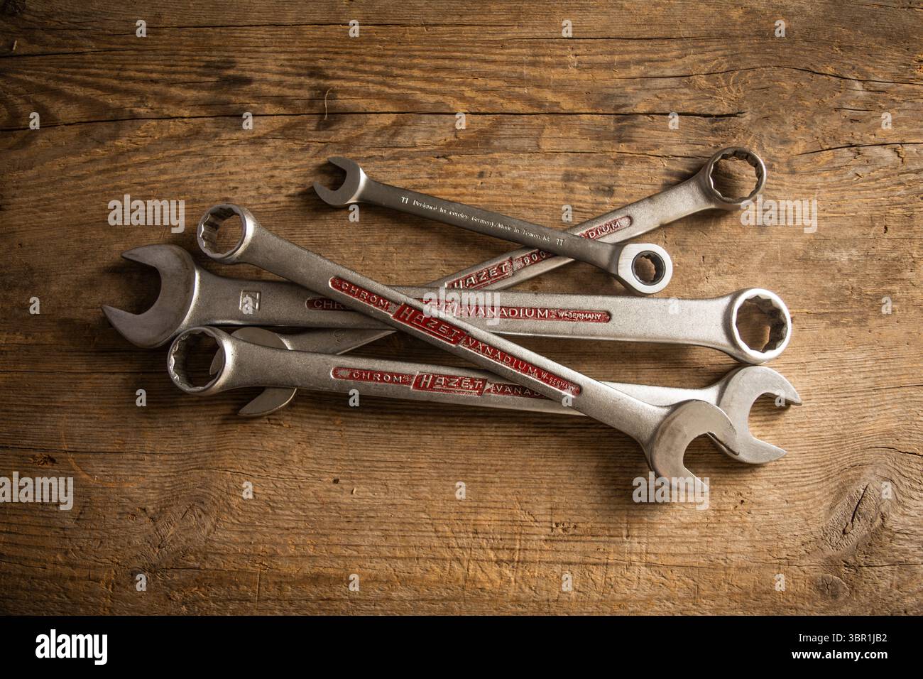 Verschiedene Chrom-Vanadium-Schraubenschlüssel, einige mit sichtbaren Markennamen, liegen verstreut auf einem rustikalen Holzhintergrund, geeignet für Reparatur- und Heimwerkerthemen. Stockfoto