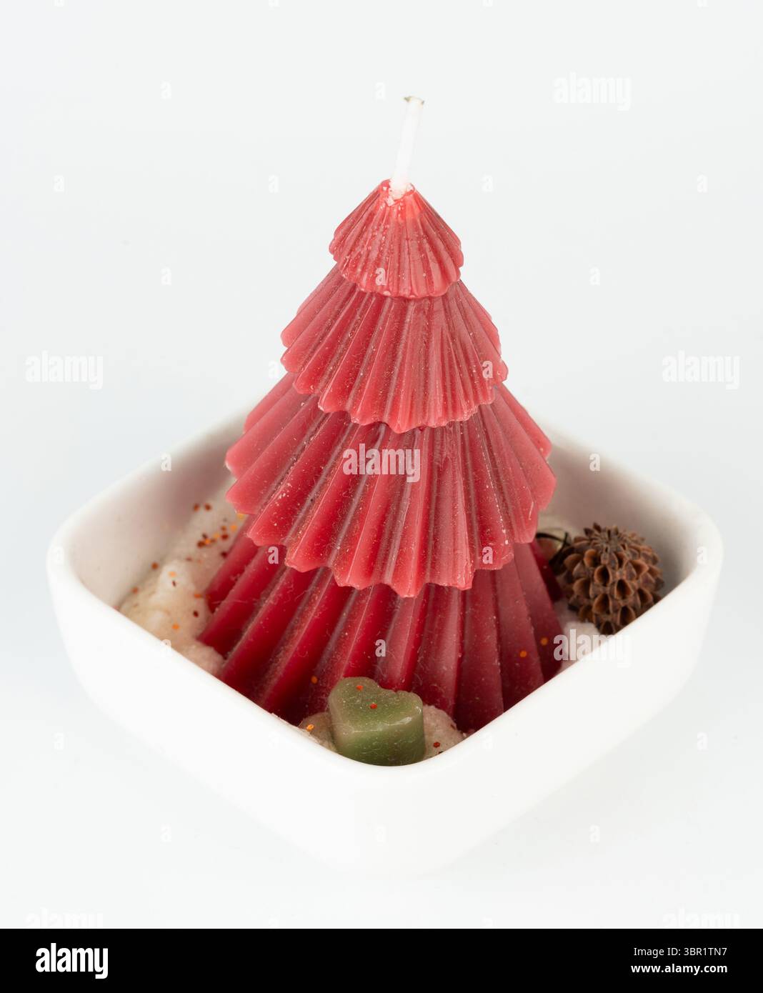 Die leuchtend rote Weihnachtsbaumkerze sitzt in einer weißen Schale mit natürlichen Dekorationen und ist bereit für die Feiertage. Stockfoto