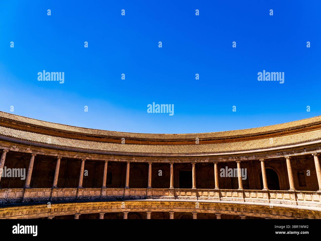 Renaissance-Steinkolonnade des Palastes Karl V. in der Alhambra, eingerahmt unter dem Kassettengang und vor einem lebendigen andalusischen Himmel Stockfoto