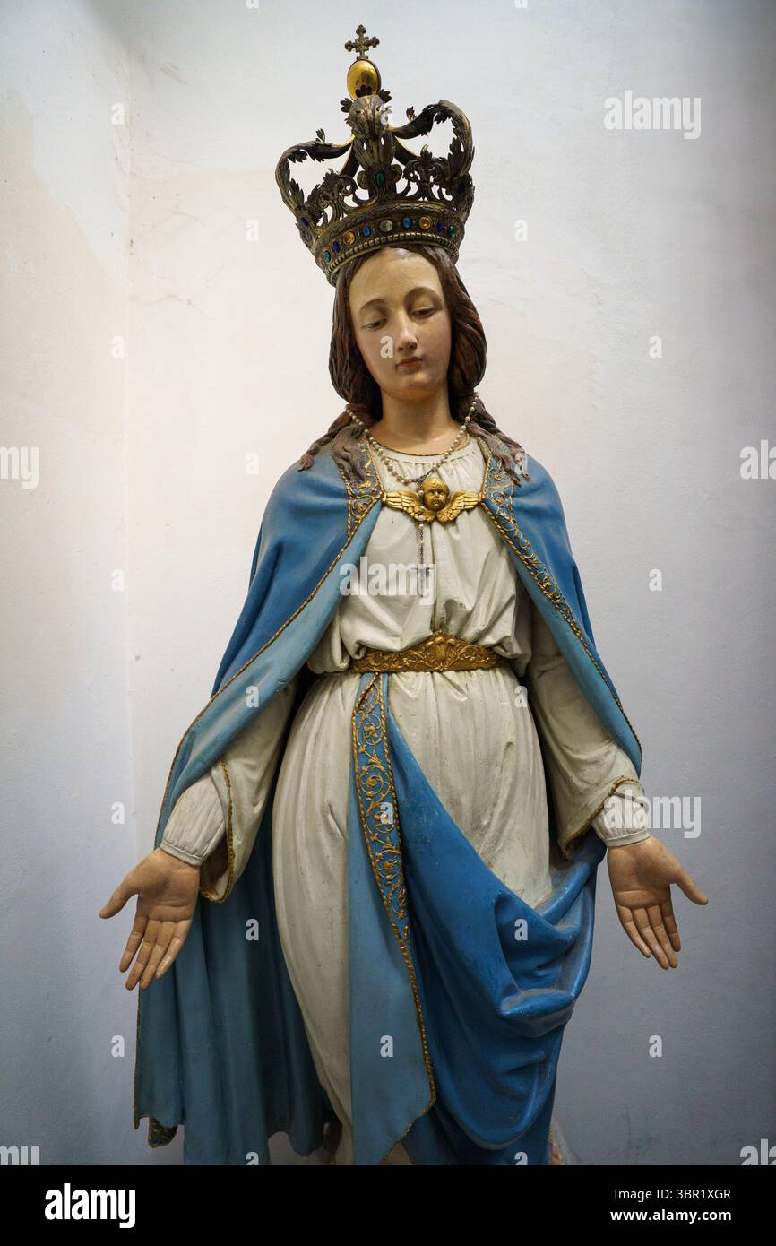 Eine Nahaufnahme einer Statue der Jungfrau Maria, die mit einer goldenen Krone verziert ist und in fließenden weißen und blauen Gewändern mit aufwändiger Goldstickerei gekleidet ist. Die Stockfoto