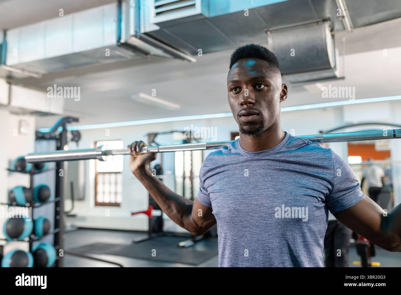 Afroamerikanischer Mann hockt mit beladener Langhantel im Fitnessstudio und zeigt einen Hocker und einen Medizinballträger. Kraft, Training, Sport, Fitness, sportlich, bsb Stockfoto