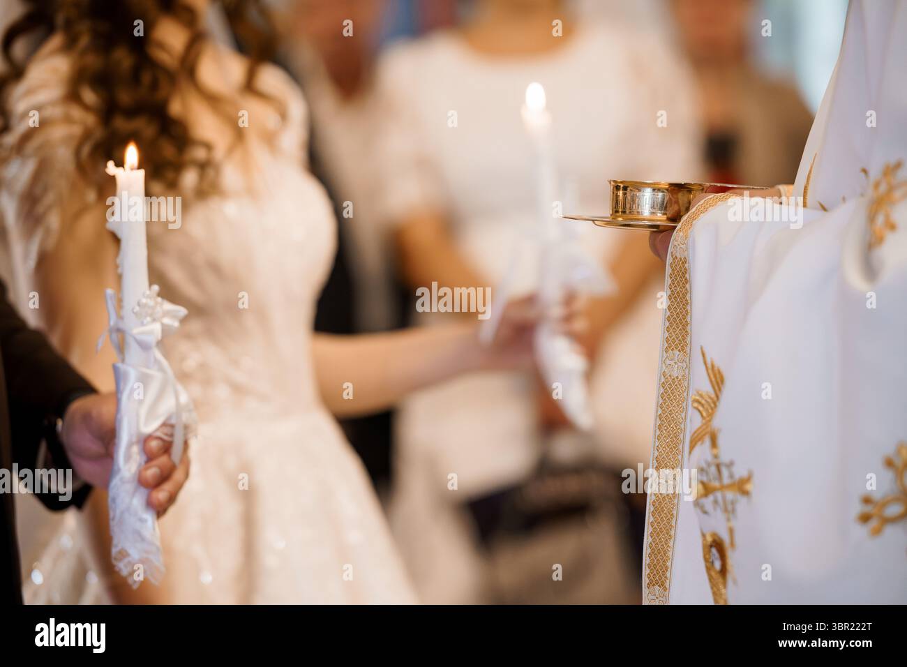Intimer Moment während einer orthodoxen christlichen Hochzeit, bei der eine Braut in weiß eine Kerze neben einem Priester während der religiösen Zeremonie zündet, Symbol Stockfoto