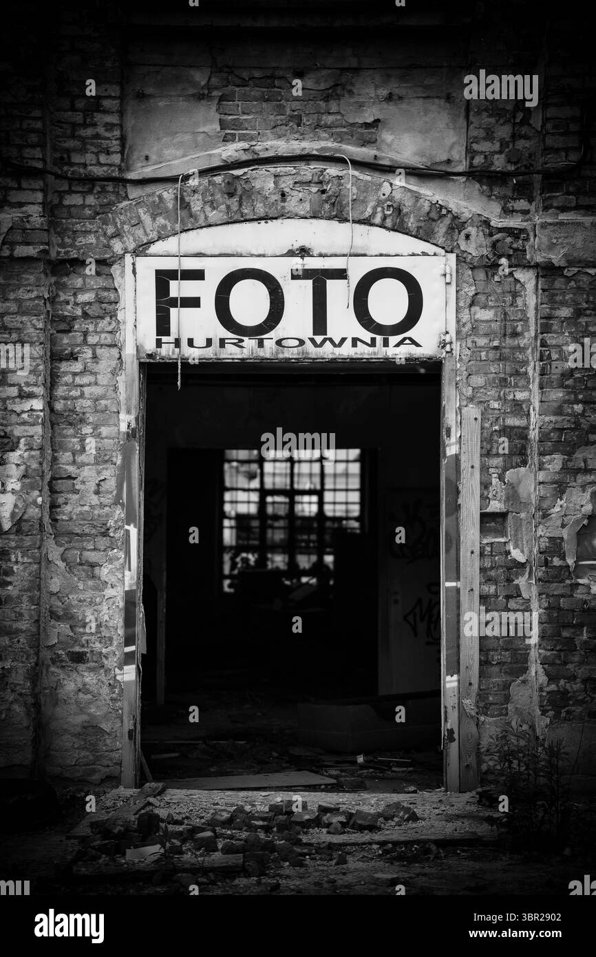Schwarzweiß-Foto eines verlassenen Gebäudeeingangs ohne Tür. Über dem Eingang ist ein großes Schild mit dem Text „Foto Hurtownia“ zu sehen Stockfoto