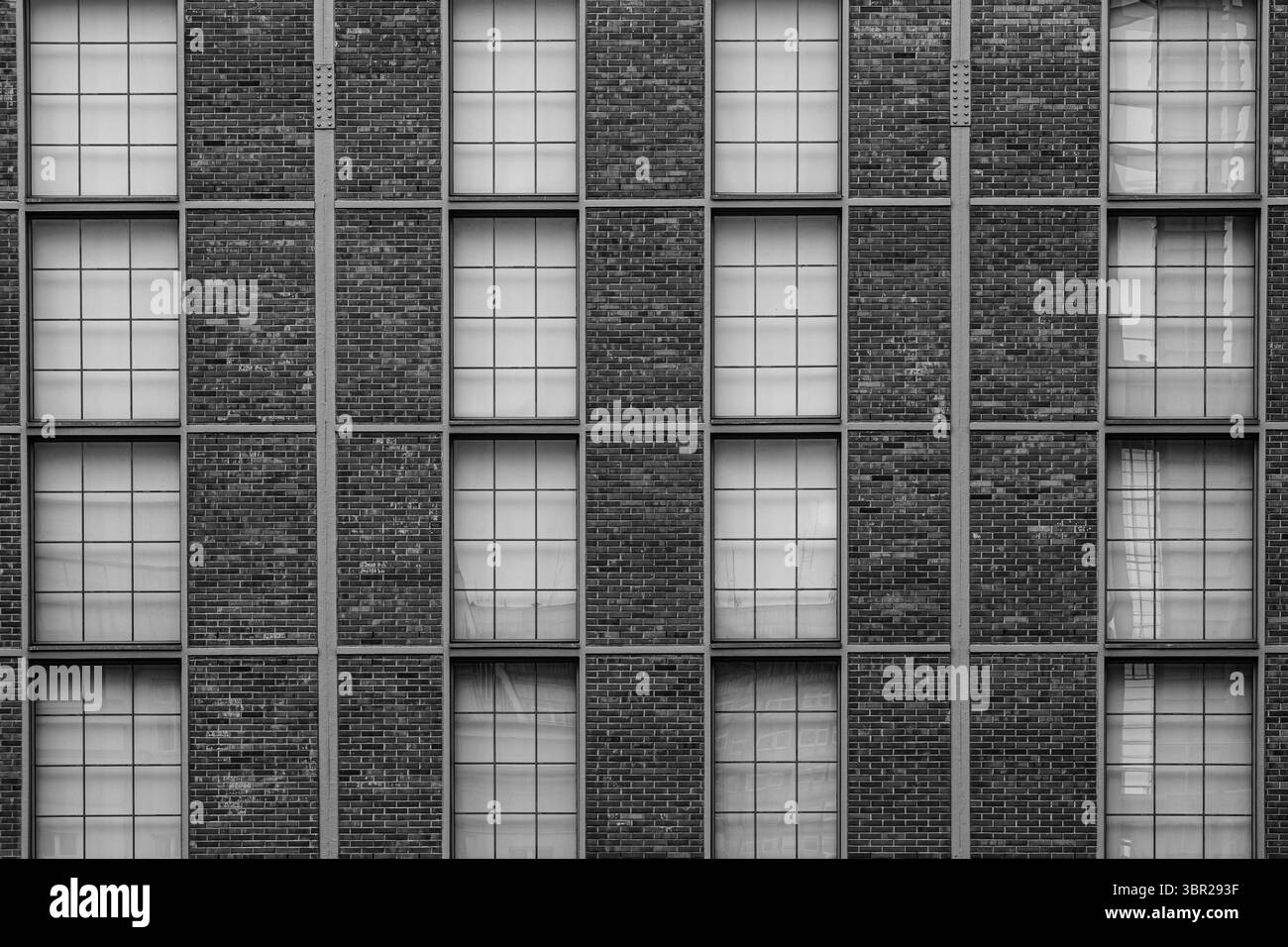 Minimalistische Fassade eines modernen Backsteingebäudes mit gleichmäßigen symmetrischen Fenstern. Schwarzweißes Architekturmuster. Stockfoto