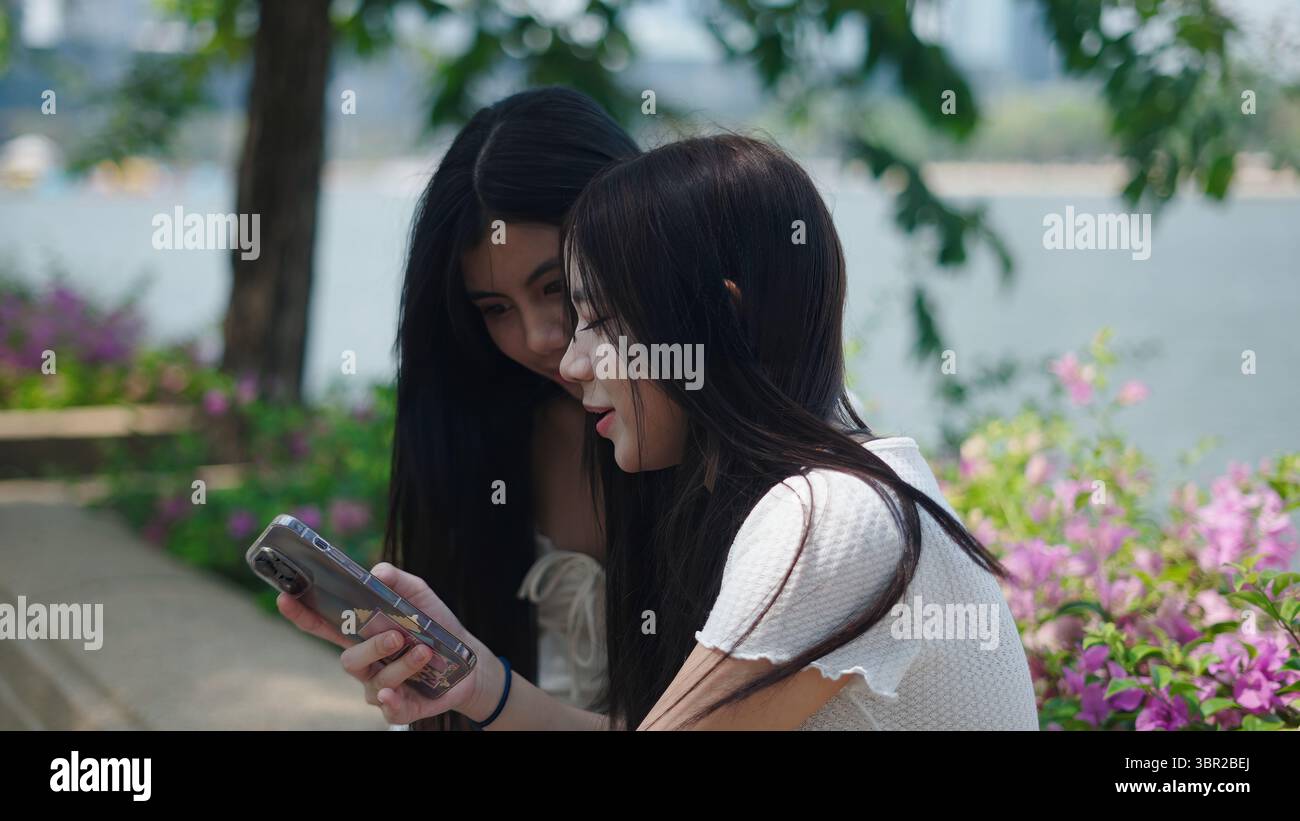 Zwei Freunde, die ein Smartphone im Park nutzen und gemeinsam Zeit im Freien genießen Stockfoto