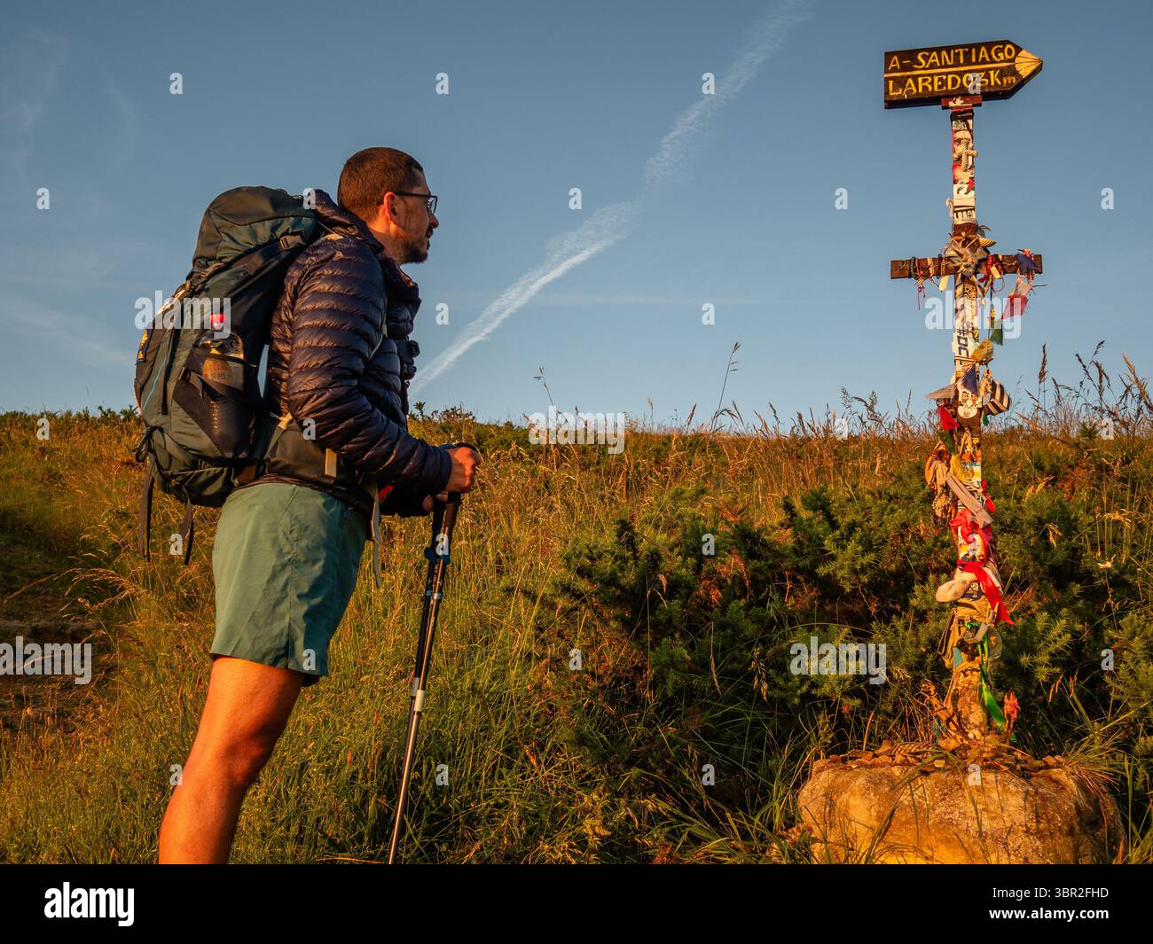Ein Pilger wirft einen Blick auf einen Pfeil, der den Weg zeigt. Der 872 km lange Nordweg, ein Zweig des Jakobsweges, beginnt in Bayonne (Frankreich) und folgt der nördlichen Küste Spaniens nach Galicien, wo er landeinwärts in Richtung Santiago de Compostela führt. Stockfoto