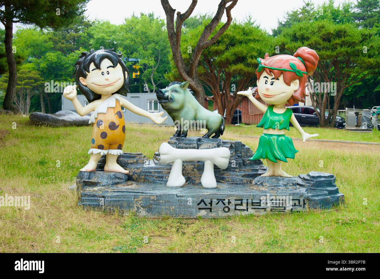 Gongju City, Südkorea - 13. Juni 2025: Statuen eines prähistorischen Jungen, Mädchens und Wildschweins im Cartoon-Stil begrüßen Besucher auf dem Eingangsrasen von SE Stockfoto