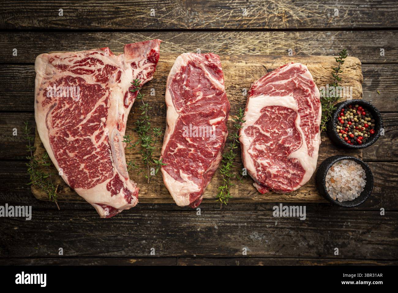 Vielfalt an frischen Raw Black Angus Prime Meat Steaks T-bone, New York, Ribeye und Gewürzen auf Holzhintergrund, Draufsicht Stockfoto
