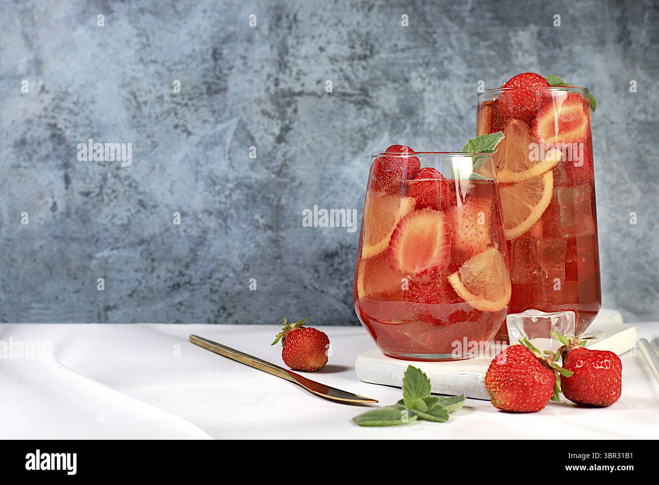 Erdbeereistee oder Pfefferminzbonbons, erfrischendes Sommergetränk. Gläser mit Beerenlimonade auf einem hellen Betontisch, Detox Diät und Gewicht Stockfoto