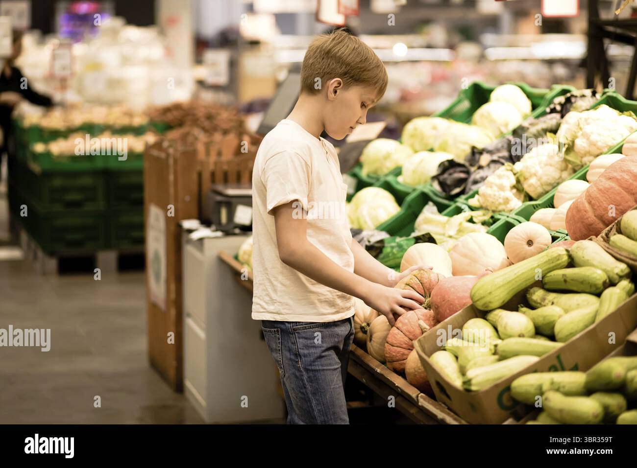Netter Teenager einkaufen für frisches Bio-Obst und Gemuese im Supermarkt. Suesser Junge haelt Kuerbis in den Haenden Stockfoto