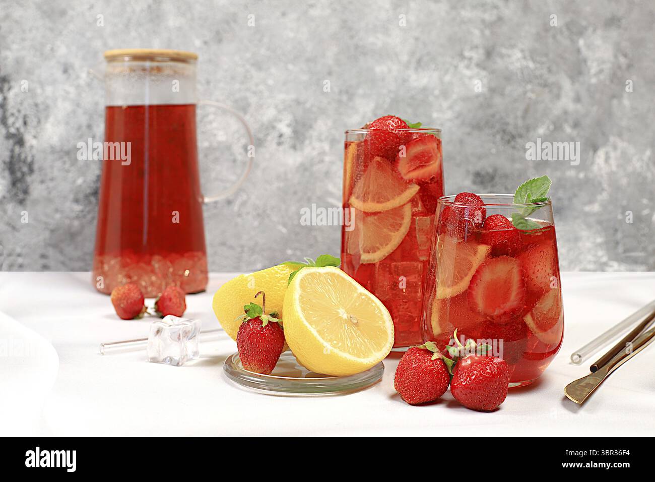 Erdbeere Iced Tea oder Minze Lemon Cocktail ist ein erfrischendes Sommergetränk. Gläser mit Beerenfrucht-Limonade auf einem hellen Betontisch, Detox-Würfel Stockfoto