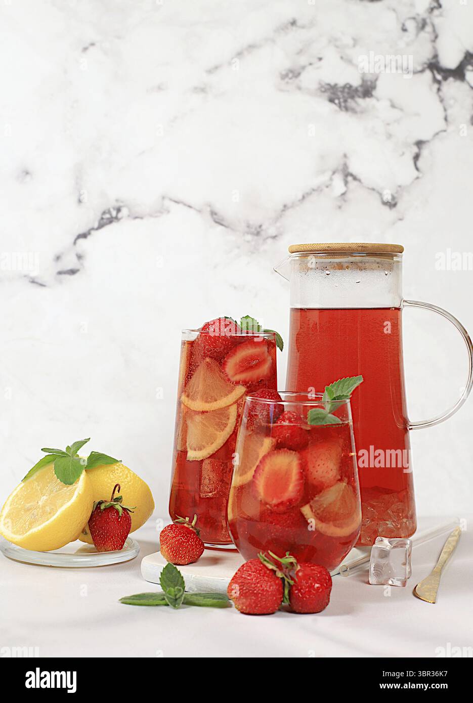 Der Smoothie mit Eiserdbeeren oder Minze-Zitronen ist ein erfrischendes Sommergetränk. Glas mit Beerenfrucht-Limonade auf einem hellen Betontisch, Detox Diät Stockfoto