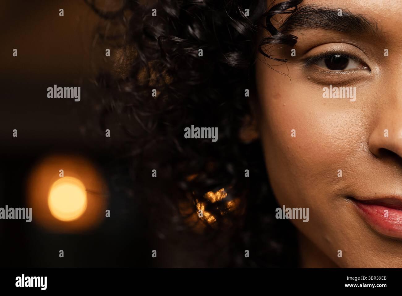 Nicht binäre afroamerikanische asiatische Person mit lockigem Haar im Studio mit Bokeh-Licht, Kopierraum Stockfoto