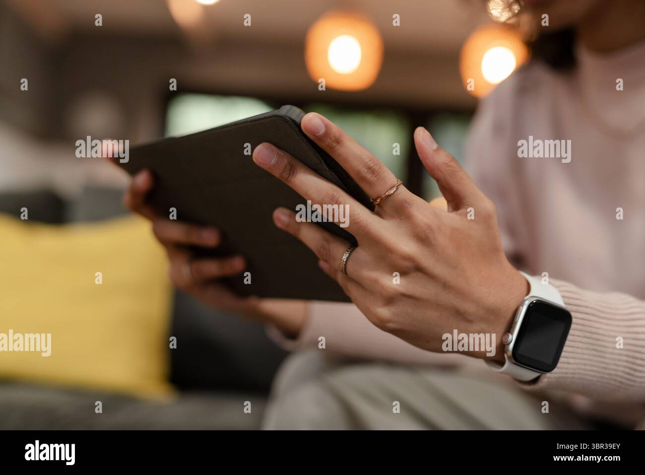 Nicht binäre Erwachsene halten die Tablette in der Schutzhülle und tragen Smartwatch auf der Couch zu Hause Stockfoto