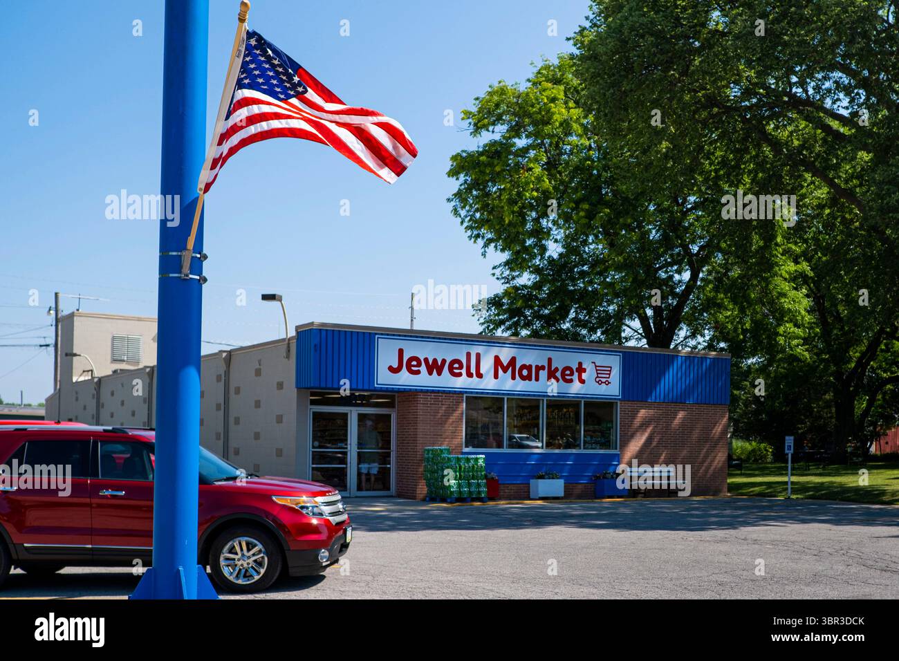 8. Juli 2020, Jewell, Iowa, USA: Eine amerikanische Flagge fliegt auf einem Lichtmast vor dem Jewell Market, dem wiedereröffneten Supermarkt in Jewell, Iowa. Der einzige Supermarkt in Jewell, einer kleinen Gemeinde im Zentrum von Iowa, wurde 2019 geschlossen. Es diente vier Gemeinden im Umkreis von 20 Meilen um Jewell. Einige Bewohner der Stadt gründeten eine Genossenschaft, um den Laden wieder zu eröffnen. Sie verkauften Aktien an die Co-op und hielten Spendenaktionen im Frühjahr ab. Die Organisatoren sammelten etwa 225.000 US-Dollar und kauften den Laden, der am 8. Juli wieder eröffnet wurde. Vor der Wiedereröffnung war Jewell sieben Monate lang eine „Essenswüste“. Der USDA-Defin Stockfoto