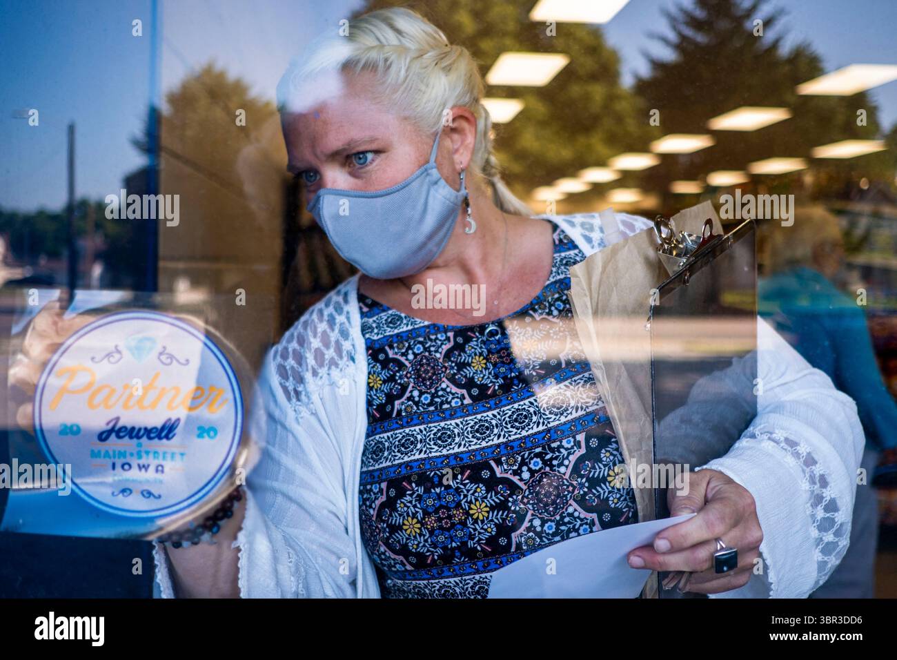 Juli 2020, Jewell, Iowa, USA: HEIDI ECKERS, der Geschäftsführer des Jewell-Büros der Main Street Iowa, bringt einen Main Street Iowa Aufkleber in die Tür des Jewell Markts. Main Street Iowa ist eine Handelskammer-Organisation für Kleinstädte in Iowa. Der einzige Supermarkt in Jewell, einer kleinen Gemeinde im Zentrum von Iowa, wurde 2019 geschlossen. Es diente vier Gemeinden im Umkreis von 20 Meilen um Jewell. Einige Bewohner der Stadt gründeten eine Genossenschaft, um den Laden wieder zu eröffnen. Sie verkauften Aktien an die Co-op und hielten Spendenaktionen im Frühjahr ab. Die Organisatoren sammelten etwa 225.000 US-Dollar und kauften die St. Stockfoto
