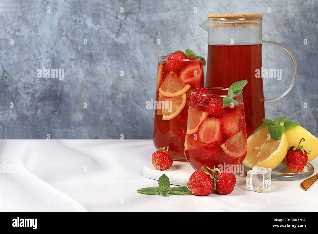 Der Smoothie mit Eiserdbeeren oder Minze-Zitronen ist ein erfrischendes Sommergetränk. Glas mit Beerenfrucht-Limonade auf einem hellen Betontisch, Detox Diät Stockfoto